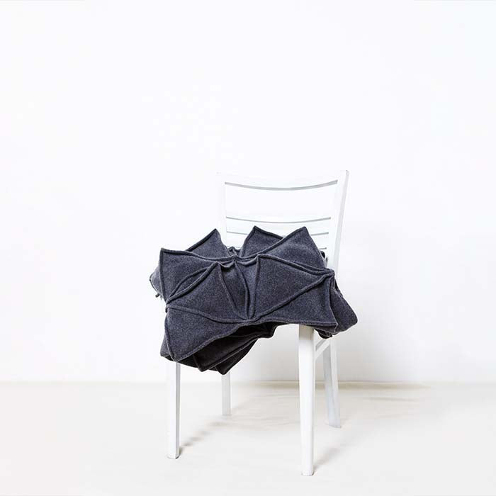 Die anthrazitfarbene Bloom Blanket der Designerin Bianca Cheng Costanzo liegt auf einem weißen Stuhl vor weißem Hintergrund